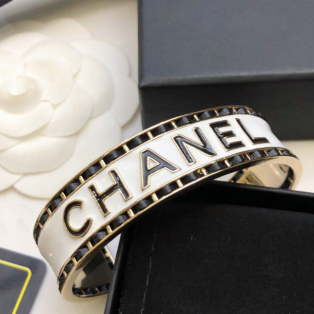 CHANEL 26S CHANEL LOGO ENAMEL CUFF BRACELET WITH BLACK TRIM IN GOLD METAL 630835